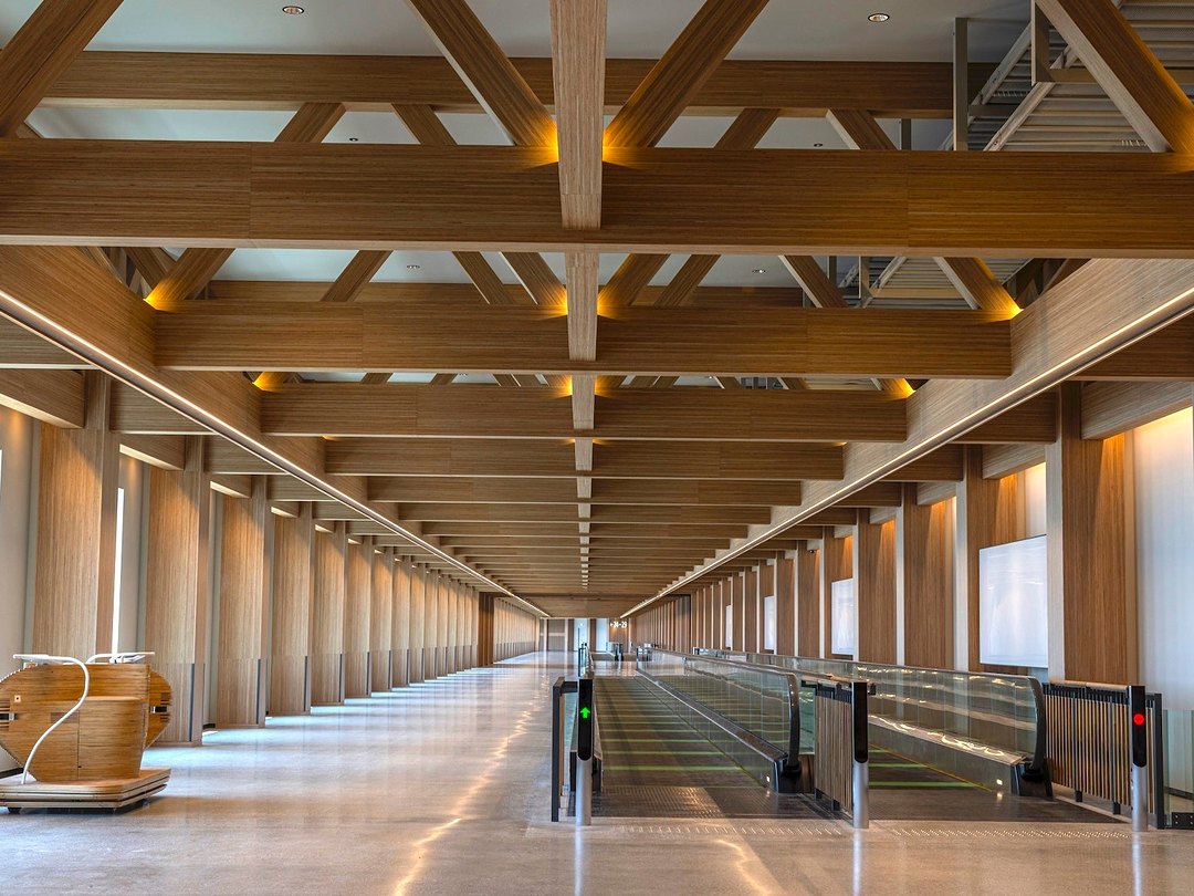 Koridor kayu panjang dengan rangka atap kayu dan travelator di satelit utara Terminal 1 Bandara Haneda